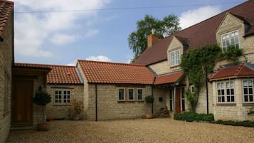 A stone building with a tiled roof, a gravel driveway, and potted plants.