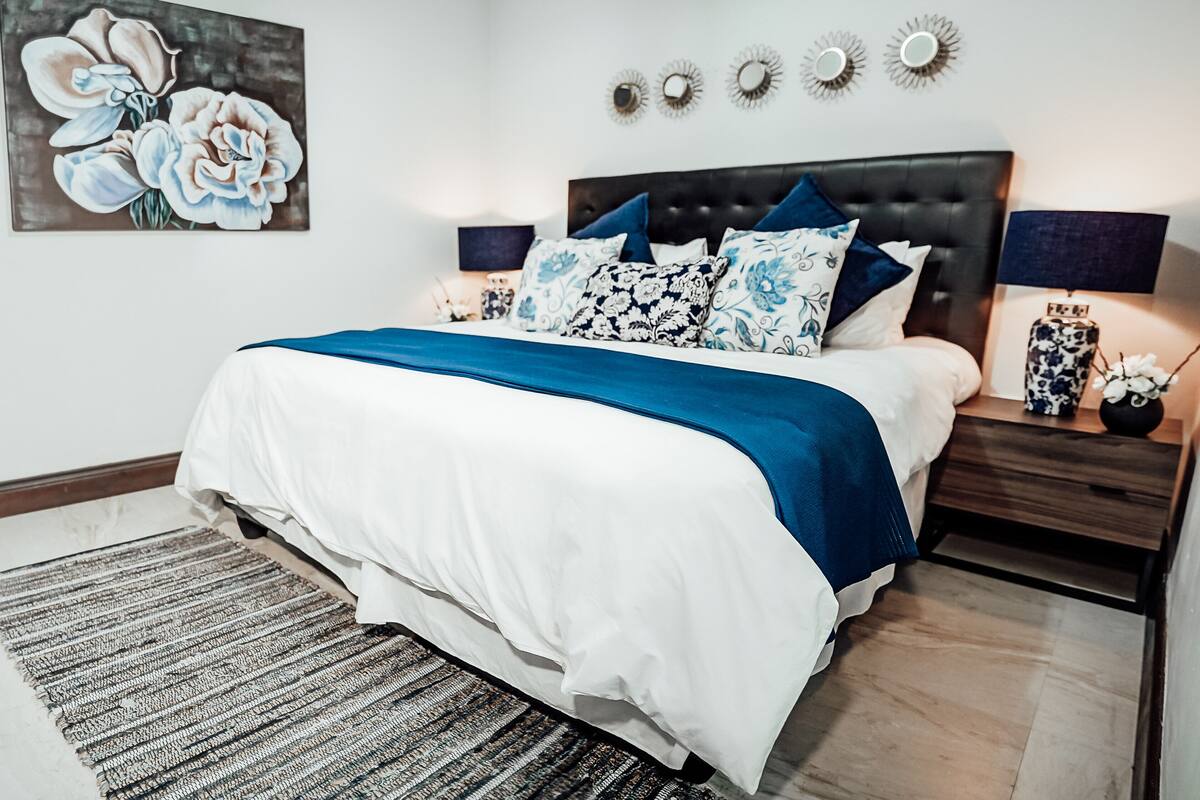 Une chambre à coucher avec un grand lit, une tête de lit, une table de chevet avec un vase et un miroir fixé au mur.