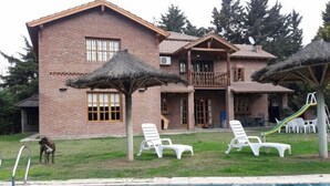 A two-story brick house with a pool, lounge chairs, and a dog.