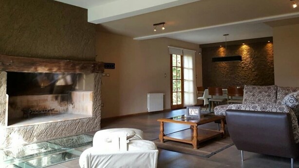 A living room with a stone fireplace, a glass coffee table, a sofa, and a patterned armchair.