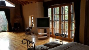 A spacious room with a large bed, a television on a stand, a rocking chair, and a bench.
