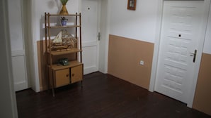 A hallway with wooden flooring, a small wooden shelf with a vase of flowers, a framed picture on the wall, and a door with a handle. - Limon Pansiyon  (Edirne)