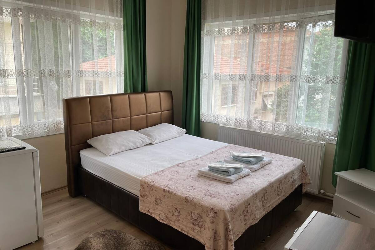 Un dormitorio con cama, mesita de noche, cómoda y ventana con cortinas.