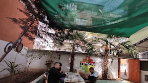 An outdoor seating area with a table and chairs, surrounded by greenery and a building facade. - Limon Pansiyon  (Edirne)