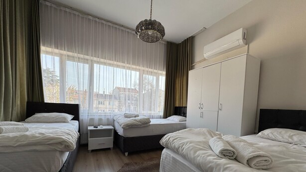 A hotel room with two beds, a wardrobe, a nightstand, and a large window with curtains. - Limon Pansiyon  (Edirne)