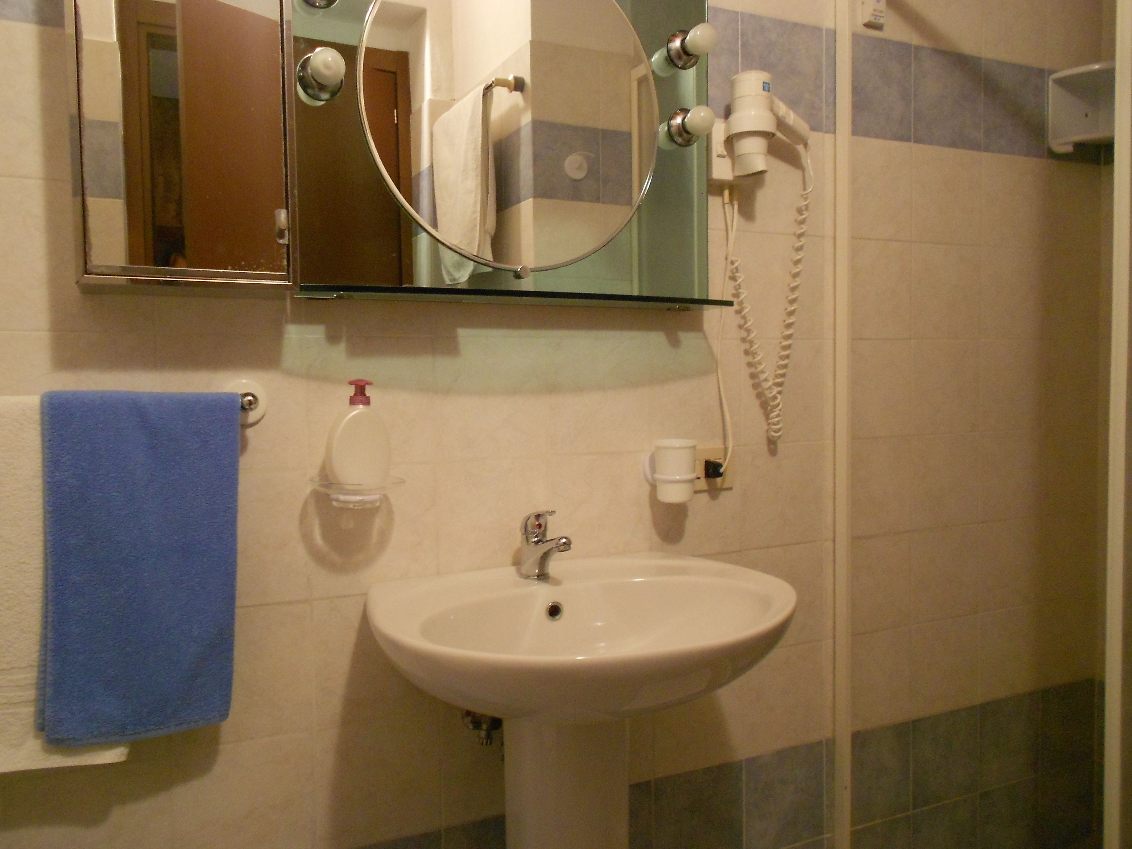 A bathroom with a white sink, a blue towel, a mirror, and a hand dryer.