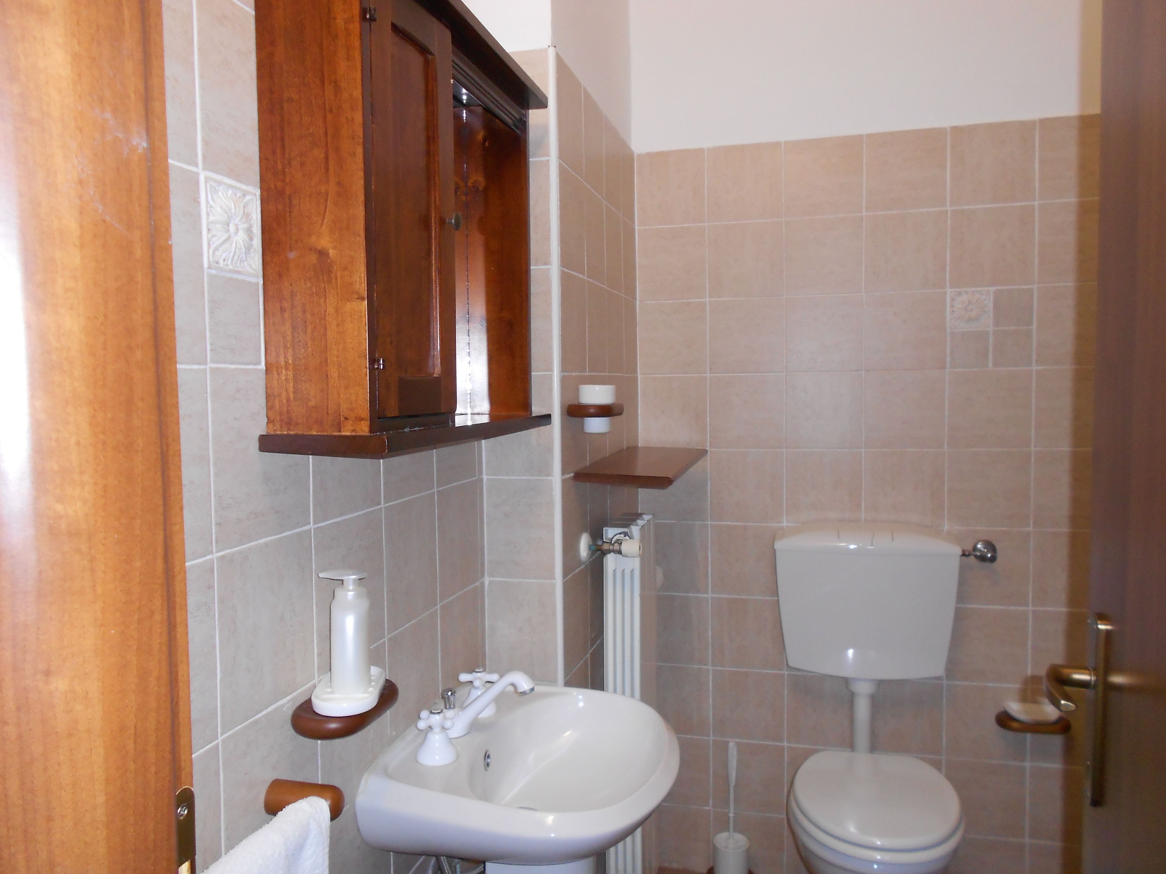 A bathroom with a wooden cabinet, a sink, a toilet, and a towel rack.
