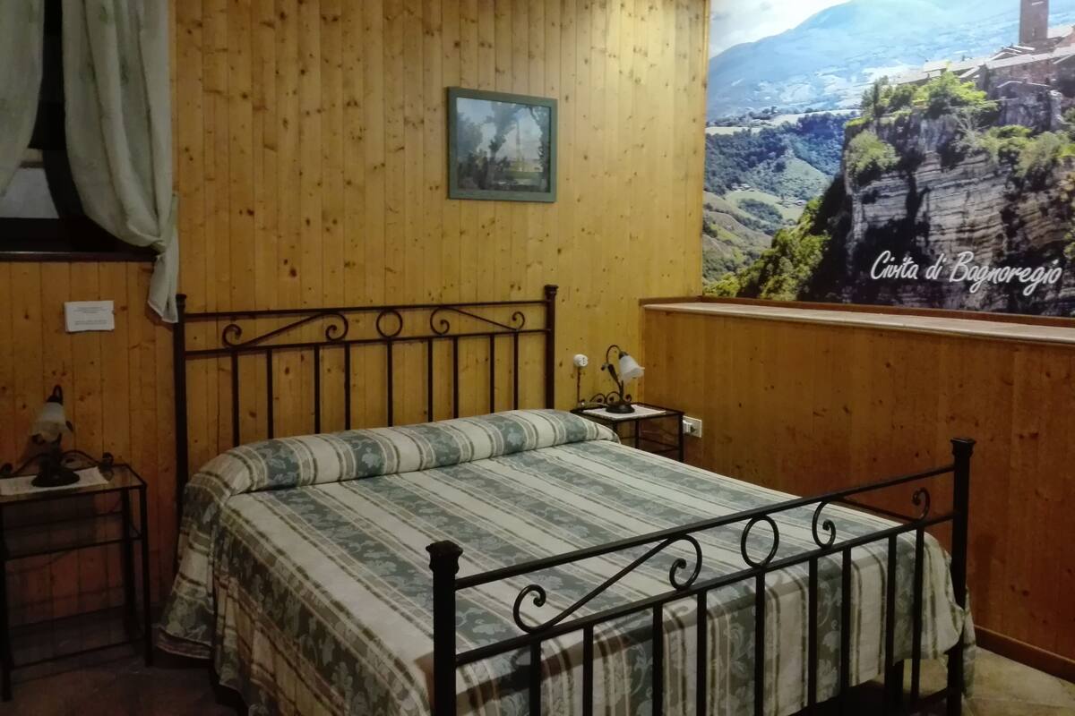 Un dormitorio con cama, mesita de noche, lámpara y ventana con vistas a un paisaje montañoso.