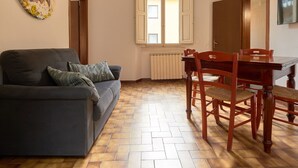 A living room with a sofa, a dining table with chairs, a radiator, and a window with shutters. - Ariento House (Florence)