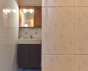 A bathroom with white marble tiles, a wooden cabinet, and a sink with a faucet. - Ariento House (Florence)