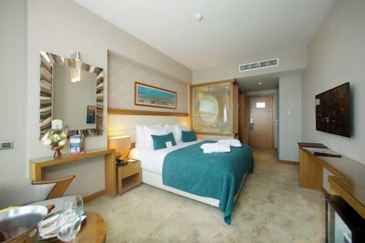 A hotel room with a bed, bedside table, lamp, and a painting on the wall.