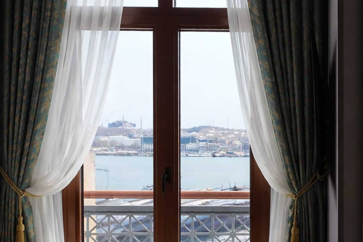 A room with a view of a body of water and a cityscape through a window with curtains.