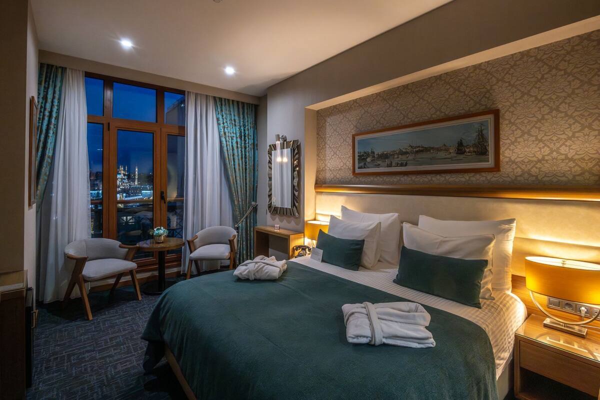 A hotel room with a large bed, a desk, a chair, and a view of a cityscape at night.