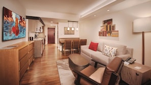 A modern living room with a sofa, a coffee table, and a leather chair. There is a kitchen area with cabinets and a dining table with chairs. - Copper Creek Villas & Cabins at Disney's Wilderness Lodge (Lake Buena Vista)