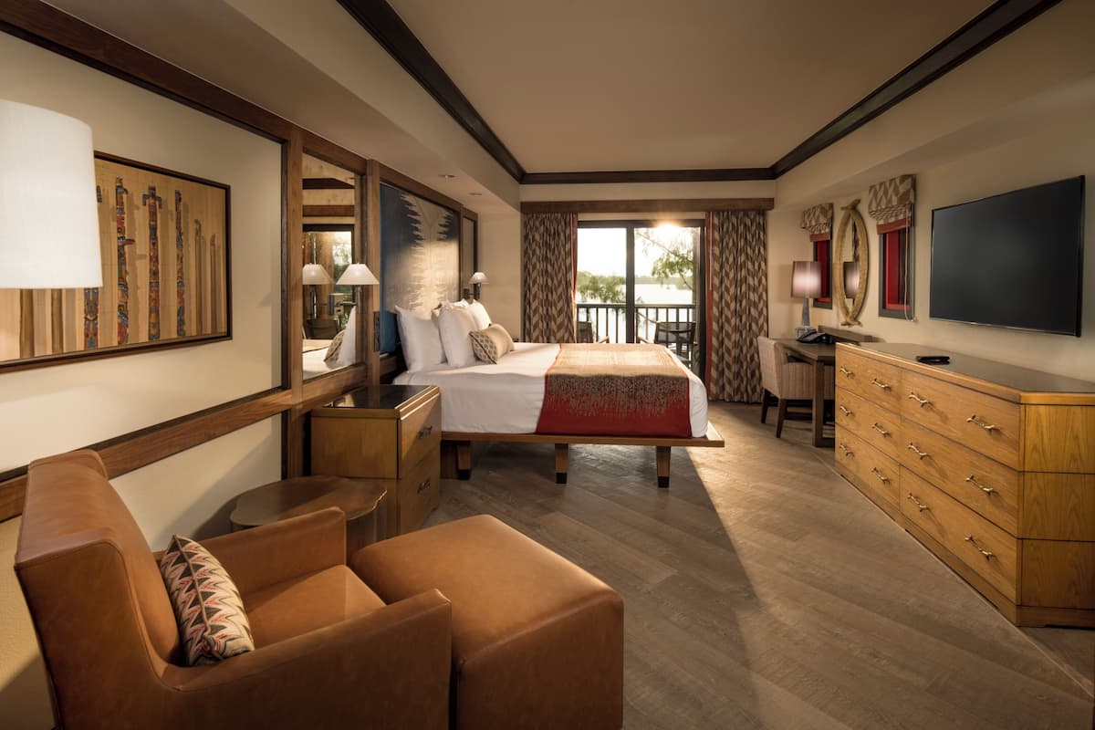 A spacious hotel room with a large bed, a sofa, a desk, and a TV.