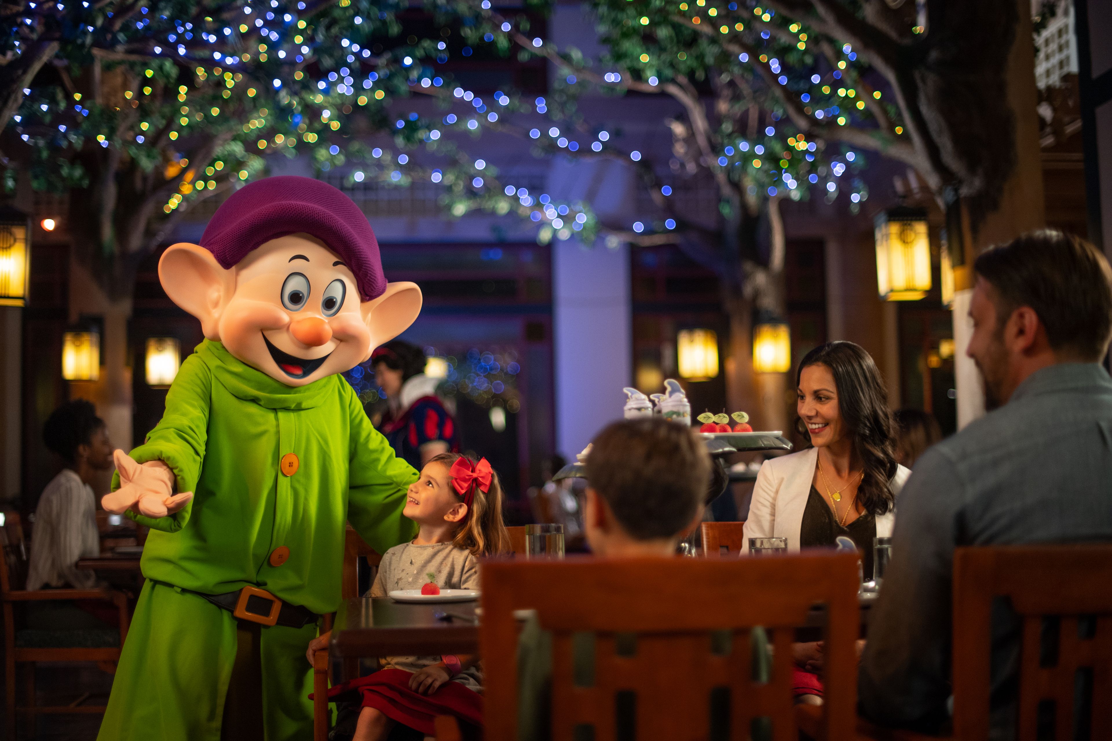 A person in a costume at a dining table with a child and adults.