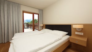 Une chambre d’hôtel avec un grand lit, une tête de lit en bois, des lampes de chevet et une vue sur les montagnes, visible à travers une porte coulissante.