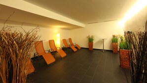 Une pièce avec quatre chaises orange disposées en rangée, un lampadaire et deux plantes en pot.