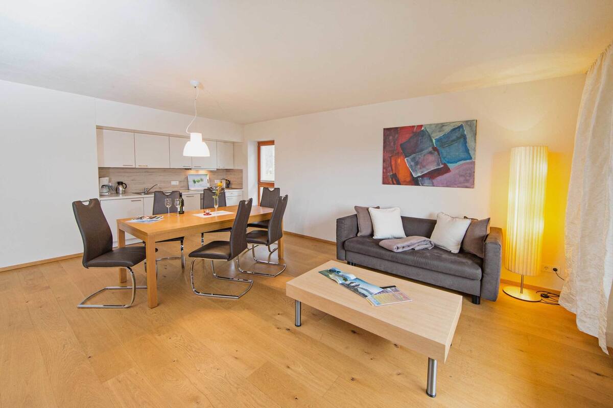 Ein modernes Wohnzimmer mit Essbereich, einer Couch, einem Couchtisch und einer Küche im Hintergrund.
