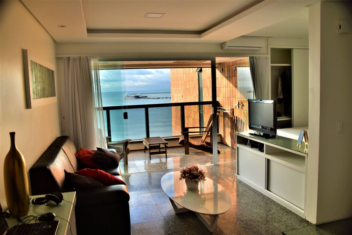 Una sala de estar moderna con vista al mar, un sofá, una mesa de centro y un televisor.