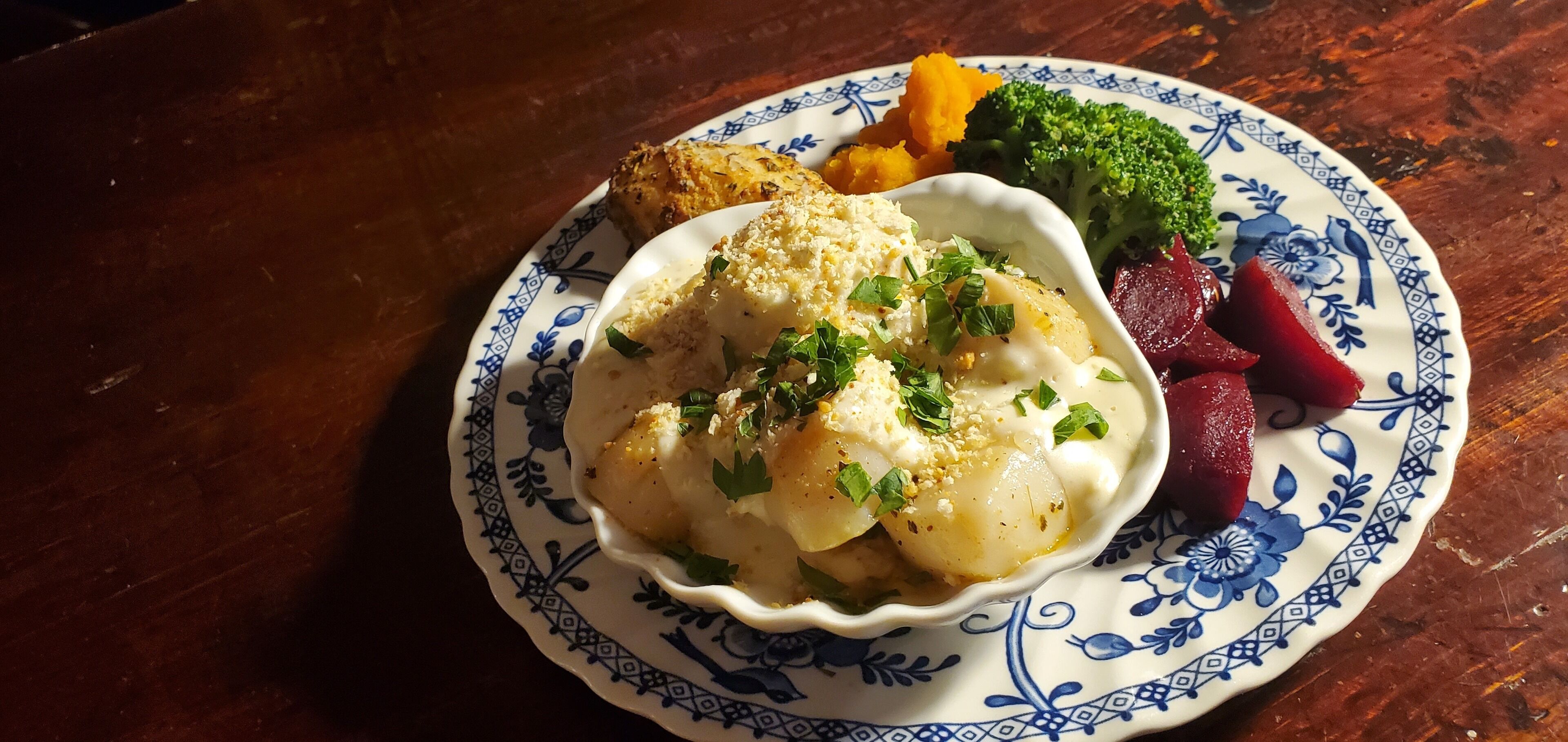 A plate with a dish of scallops, beets, and broccoli on a patterned plate.