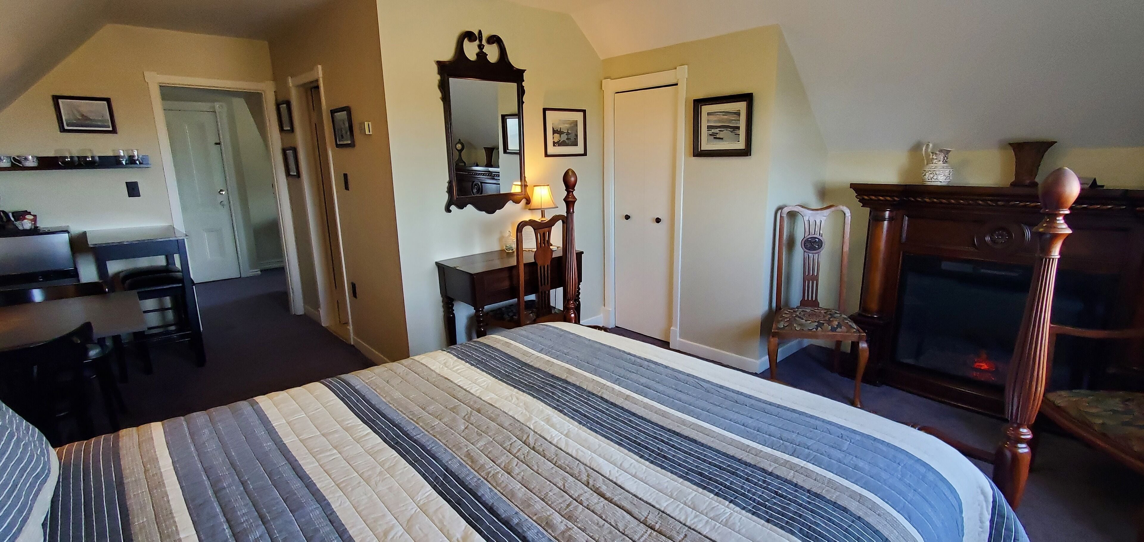 A bedroom with a bed, a dresser, a chair, a mirror, and a fireplace.