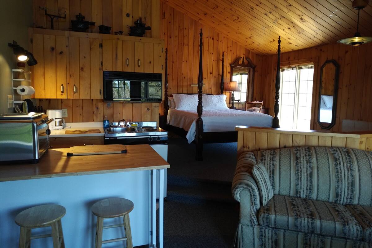 A wooden cabin interior with a bed, a dining area, and a kitchen.