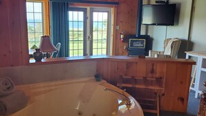 A wooden cabin room with a large bathtub, a television, and a view of the outdoors. - Amherst Shore Country Inn (Lorneville)