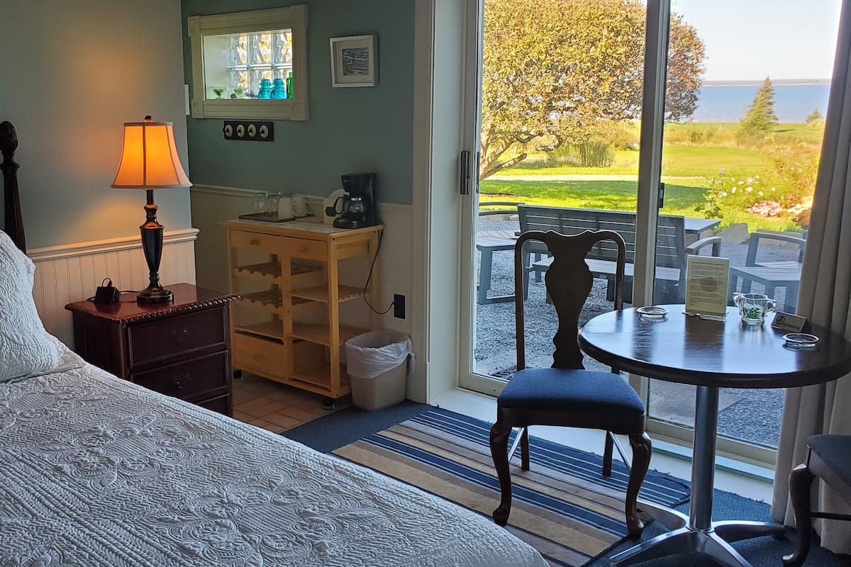 A hotel room with a bed, a lamp, a small table with chairs, and a view of the outdoors.