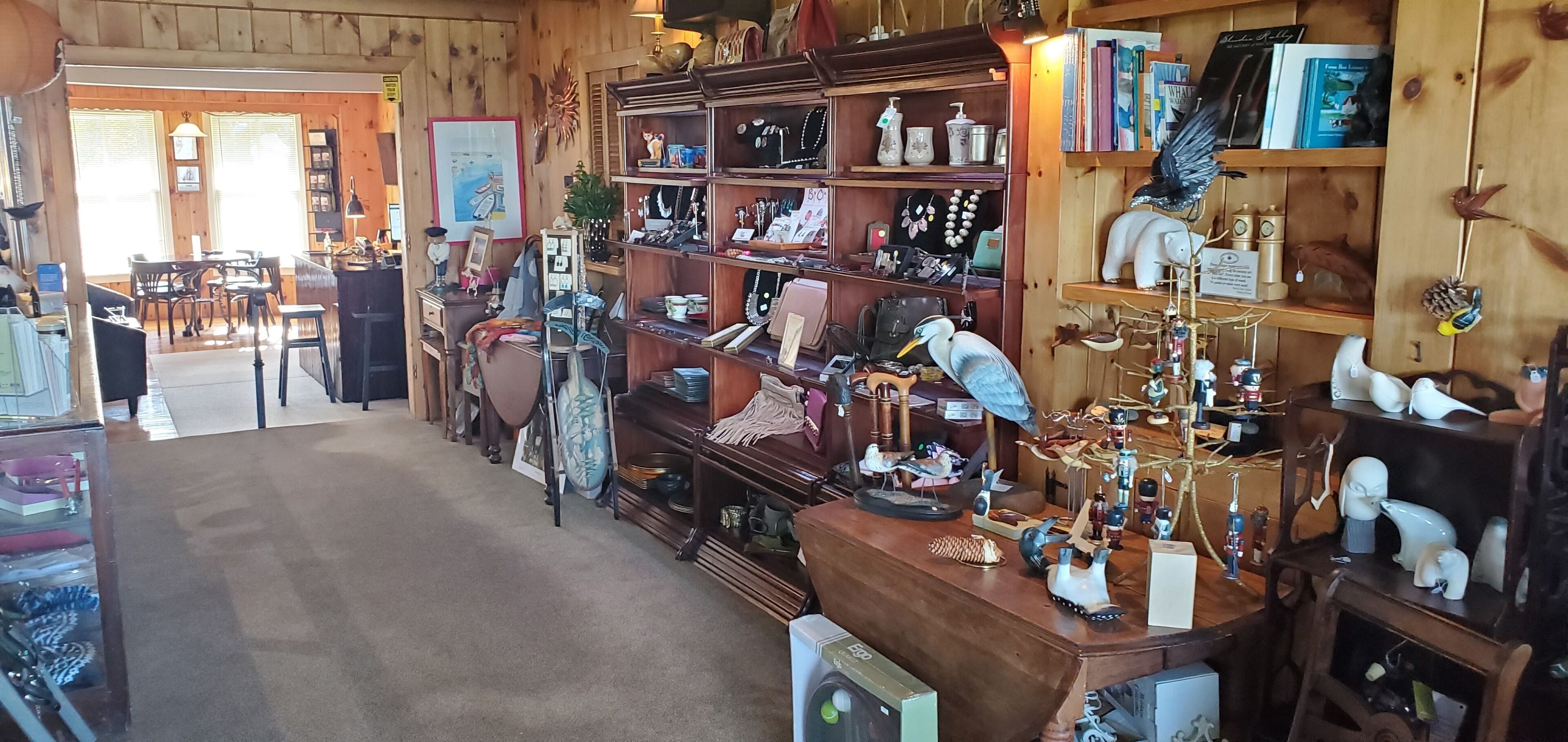 Une pièce chaleureuse aux murs en bois et aux étagères remplies de divers objets. On y trouve un bureau avec une chaise, une petite table avec une lampe, et une bibliothèque contenant des livres et des objets décoratifs.