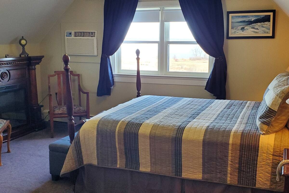A bedroom with a bed, bedside lamps, a dresser, a chair, a window with curtains, and a painting on the wall.