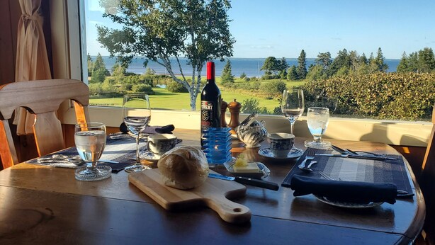 A table set for a meal with a bottle of wine, glasses, a bread roll, and cutlery. - Amherst Shore Country Inn (Lorneville)