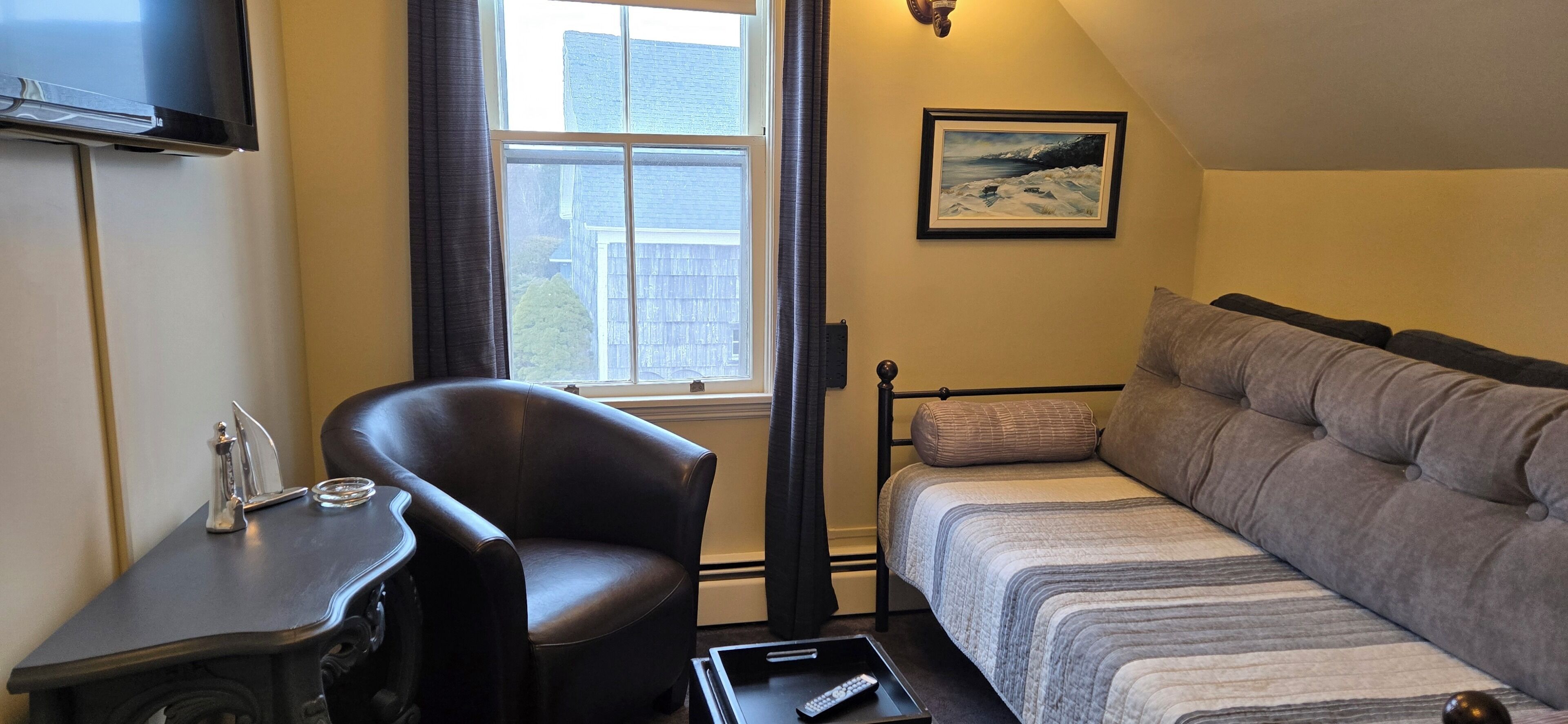 Ein kleines, gemütliches Zimmer mit einem Bett, einem Sessel, einem Schreibtisch und einem Fernseher.