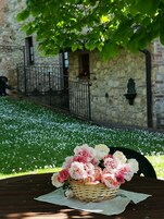 Una cesta de mimbre con flores sobre una mesa, con un muro de piedra y un balcón al fondo.