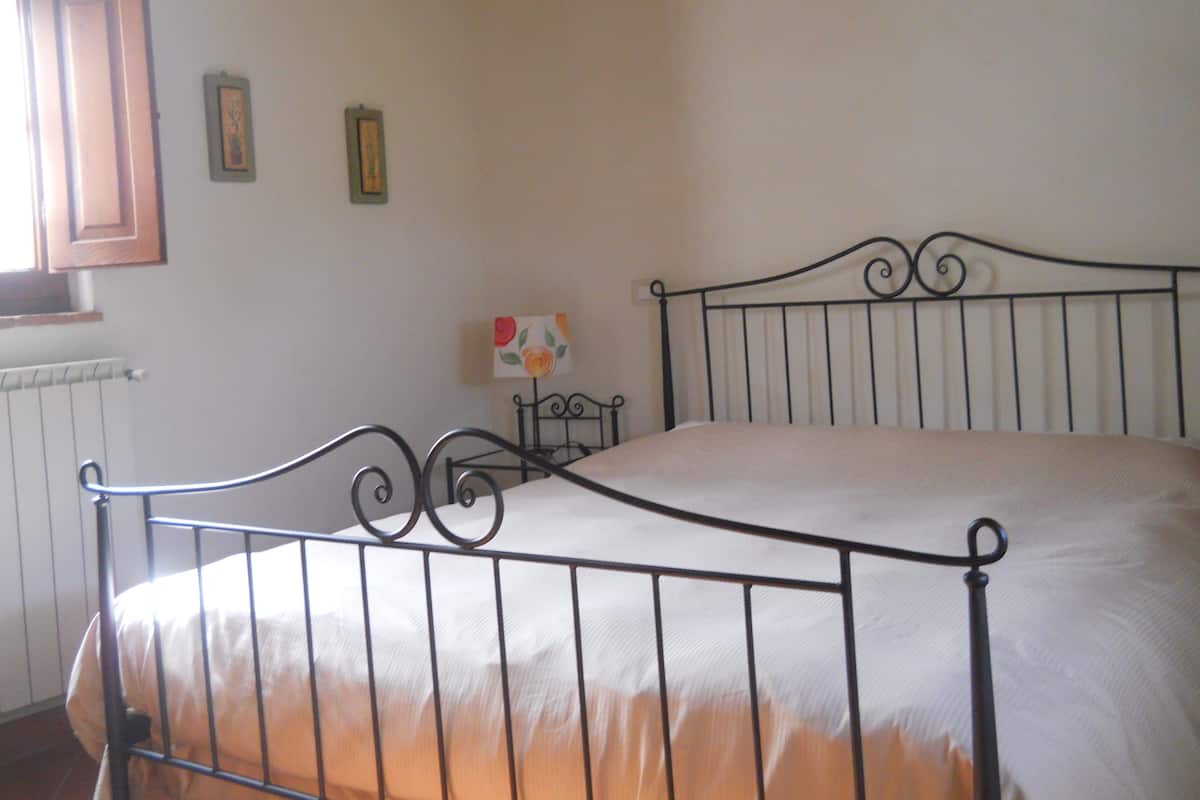 Un dormitorio con estructura de cama de metal, un radiador y dos cuadros en la pared.