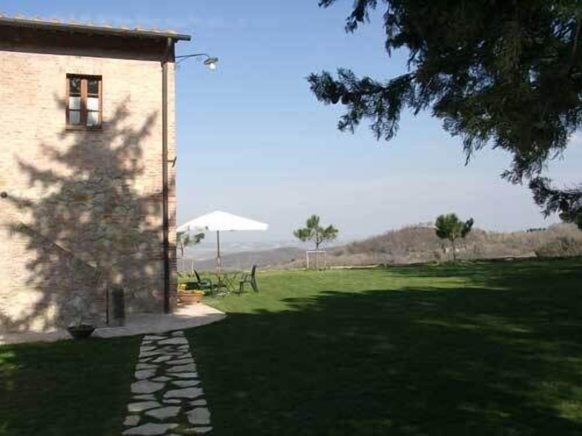 A stone building with a small window, a paved pathway leading to a grassy area, and a white umbrella.