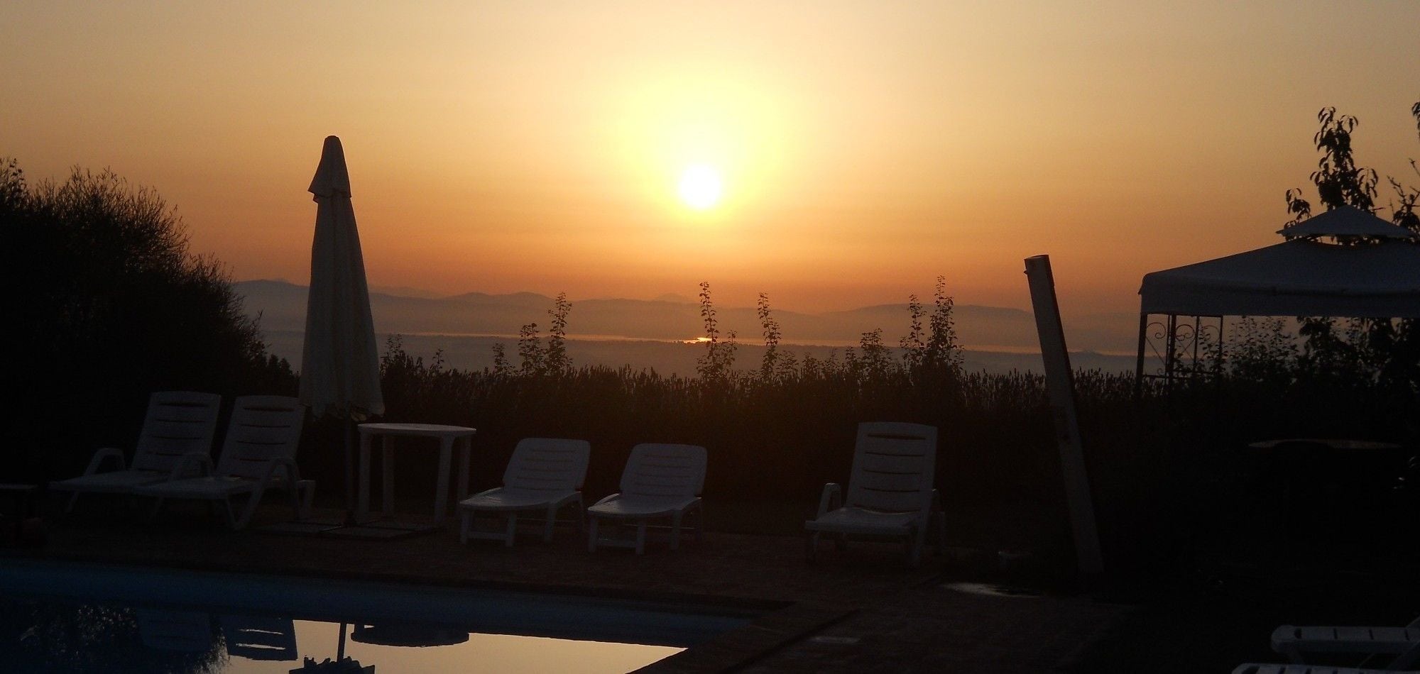 A sunset view with lounge chairs and a pool.