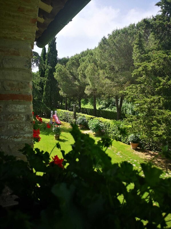 A garden with a variety of plants and trees, a clear sky, and a stone structure in the foreground.