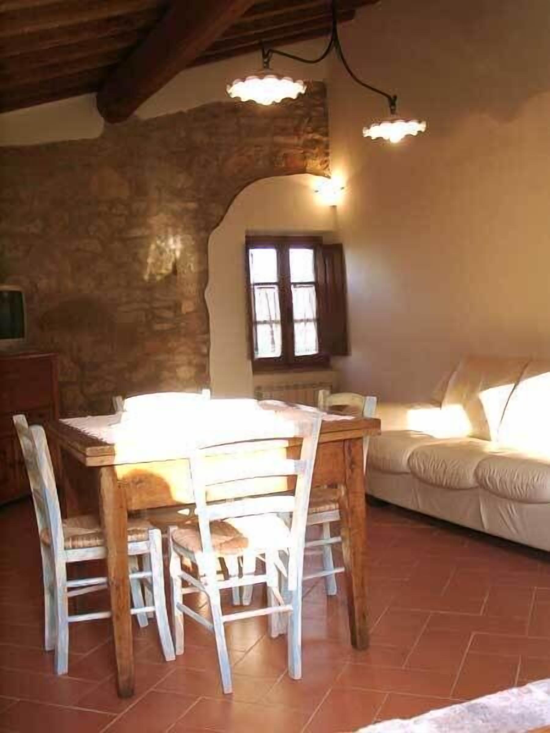 Un comedor rústico con una mesa y sillas de madera, una pared de piedra y una ventana con cortinas.