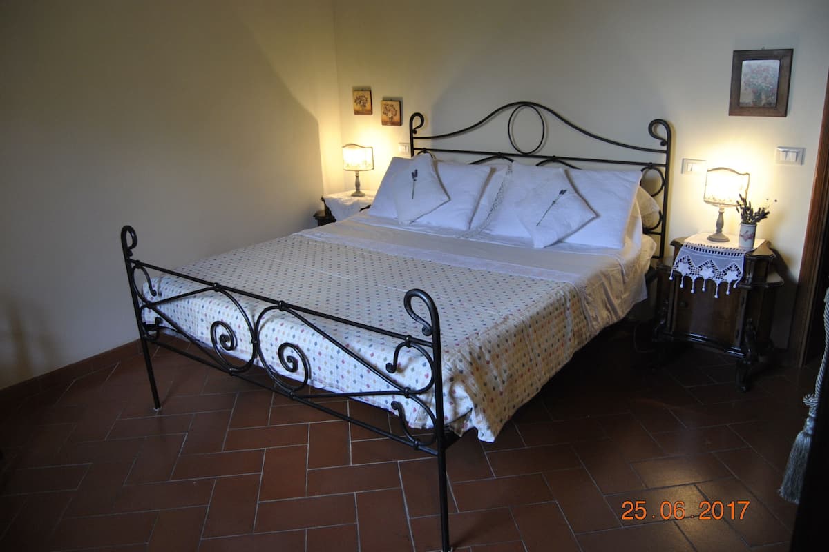 Una cama con estructura metálica, ropa de cama blanca y dos lámparas de noche.