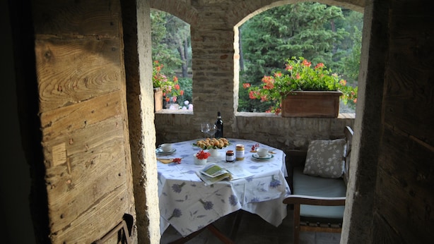 A rustic wooden table set with a white tablecloth, a bottle, and a bowl of fruit. - Frateria Di San Benedetto (Montepulciano)