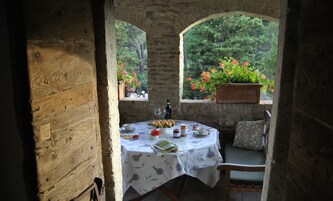 A rustic wooden table set with a white tablecloth, a bottle, and a bowl of fruit.