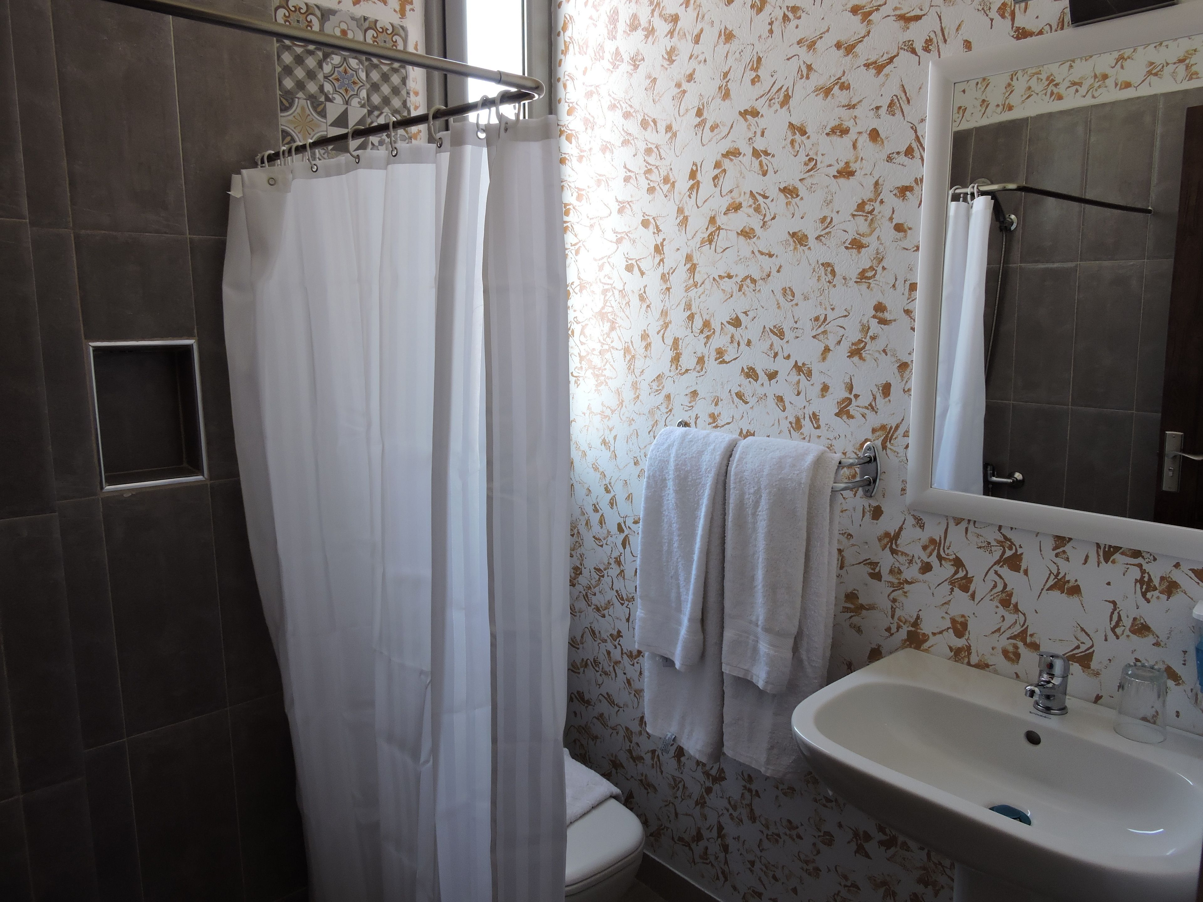 A bathroom with a shower curtain, a toilet, a sink, and a mirror.