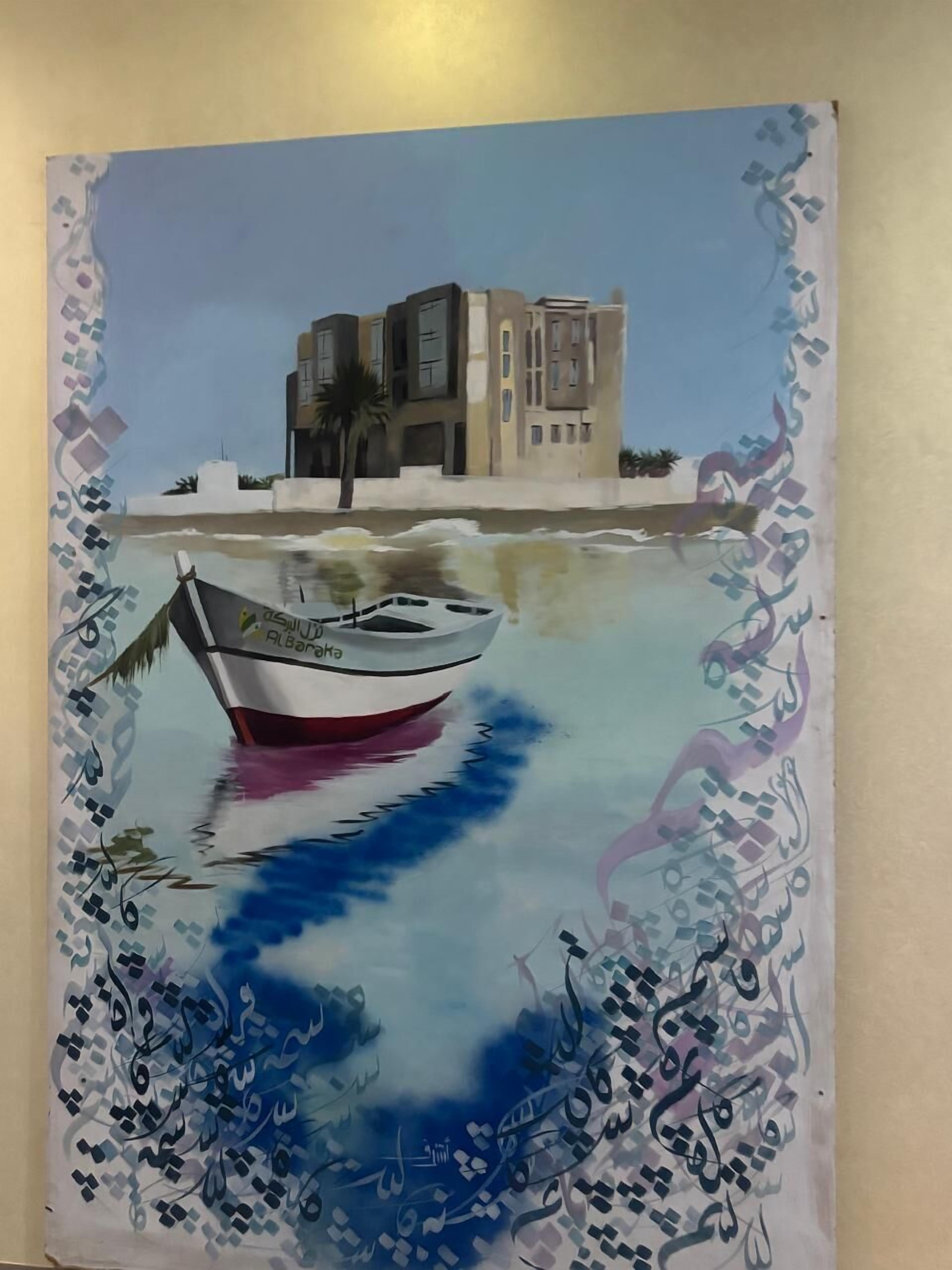 Un bateau orné de caractères arabes sur sa coque est amarré dans des eaux calmes, avec un bâtiment visible en arrière-plan.