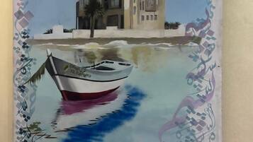 Un bateau orné de caractères arabes sur sa coque est amarré dans des eaux calmes, avec un bâtiment visible en arrière-plan.