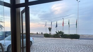 A paved area with flags, a car, and a building entrance. - Hôtel Al Baraka (Fatou)