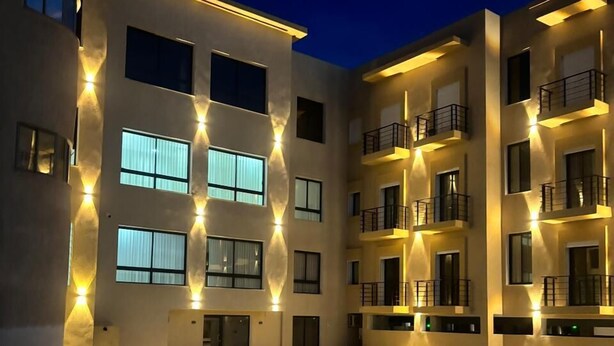 A modern multi-story building with illuminated windows and balconies, a courtyard with a pool, and a flat roof. - Hôtel Al Baraka (Fatou)