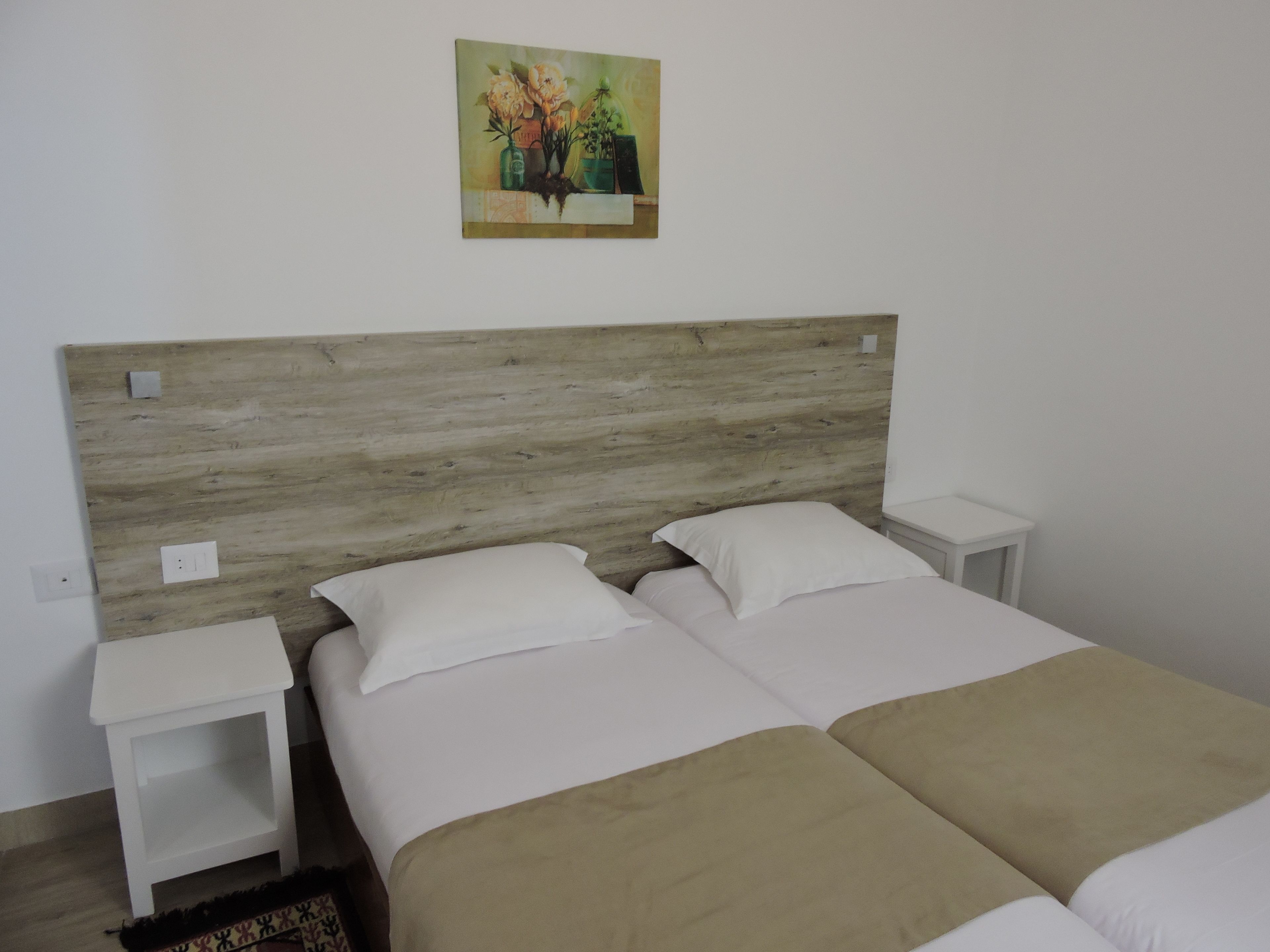 Una habitación con cabecera de madera, dos camas con ropa blanca y una mesita de noche a cada lado.