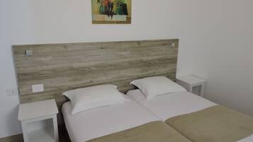Una habitación con cabecera de madera, dos camas con ropa blanca y una mesita de noche a cada lado.