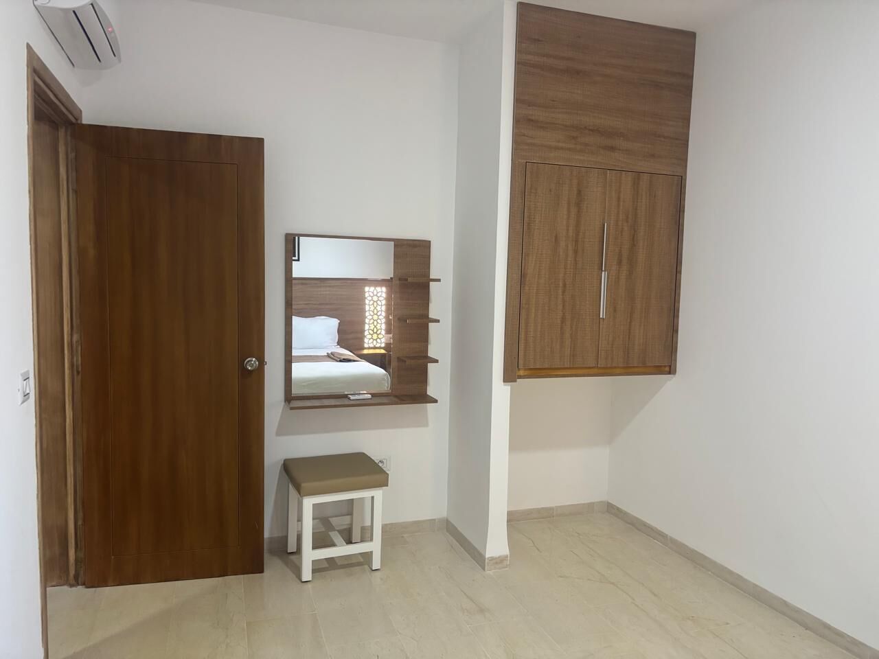 A bedroom with a wooden wardrobe, a bedside table, and a mirror.